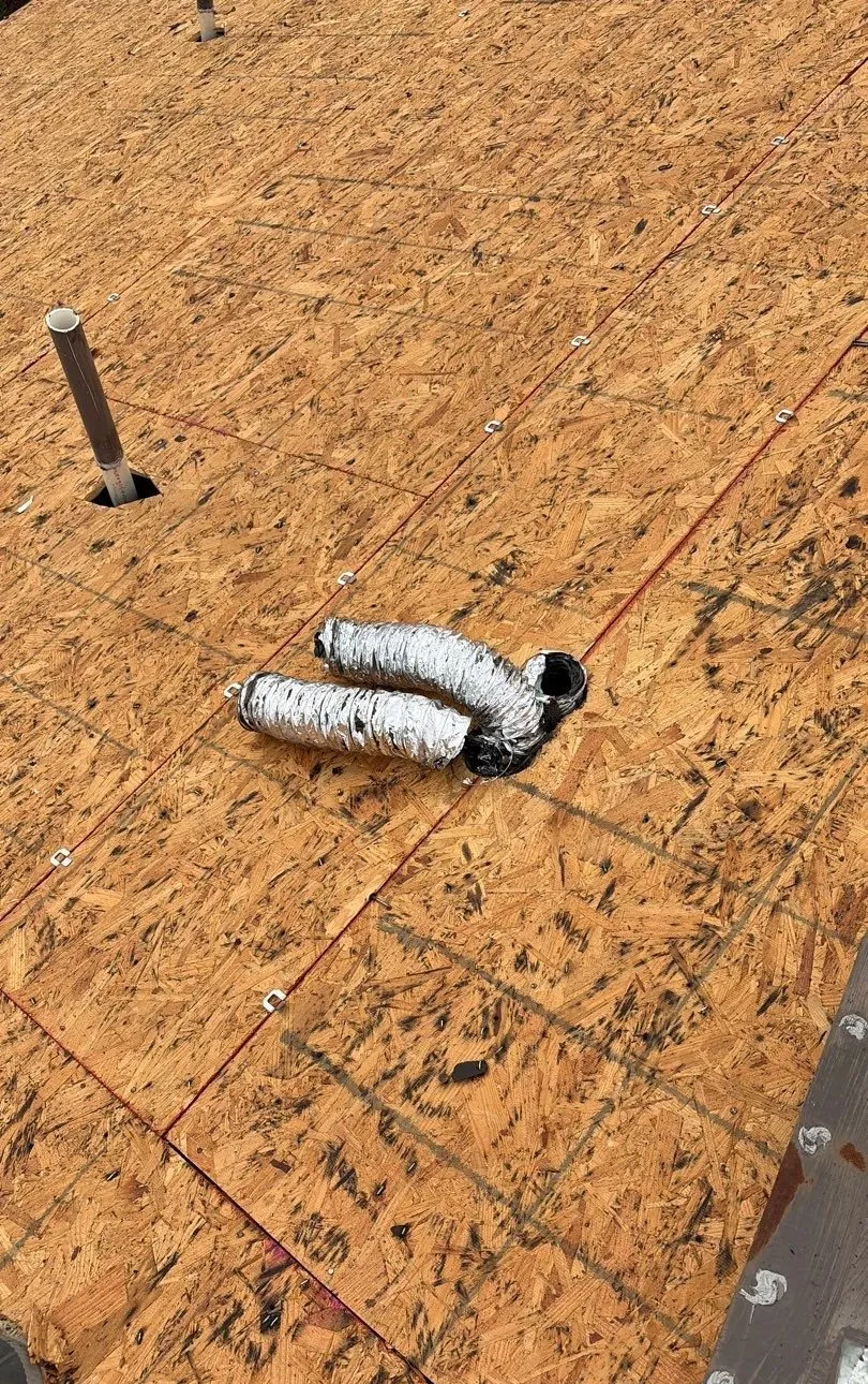 Bare roof deck after tear-off with two flexible foil exhaust ducts coming out of a single hole