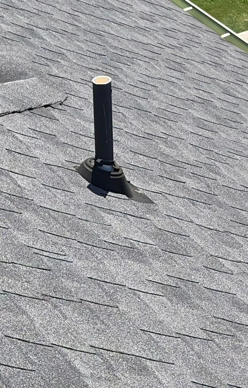 Plumbing vent pipe on a gray shingle roof with a dried-out, cracked rubber pipe jack at its base