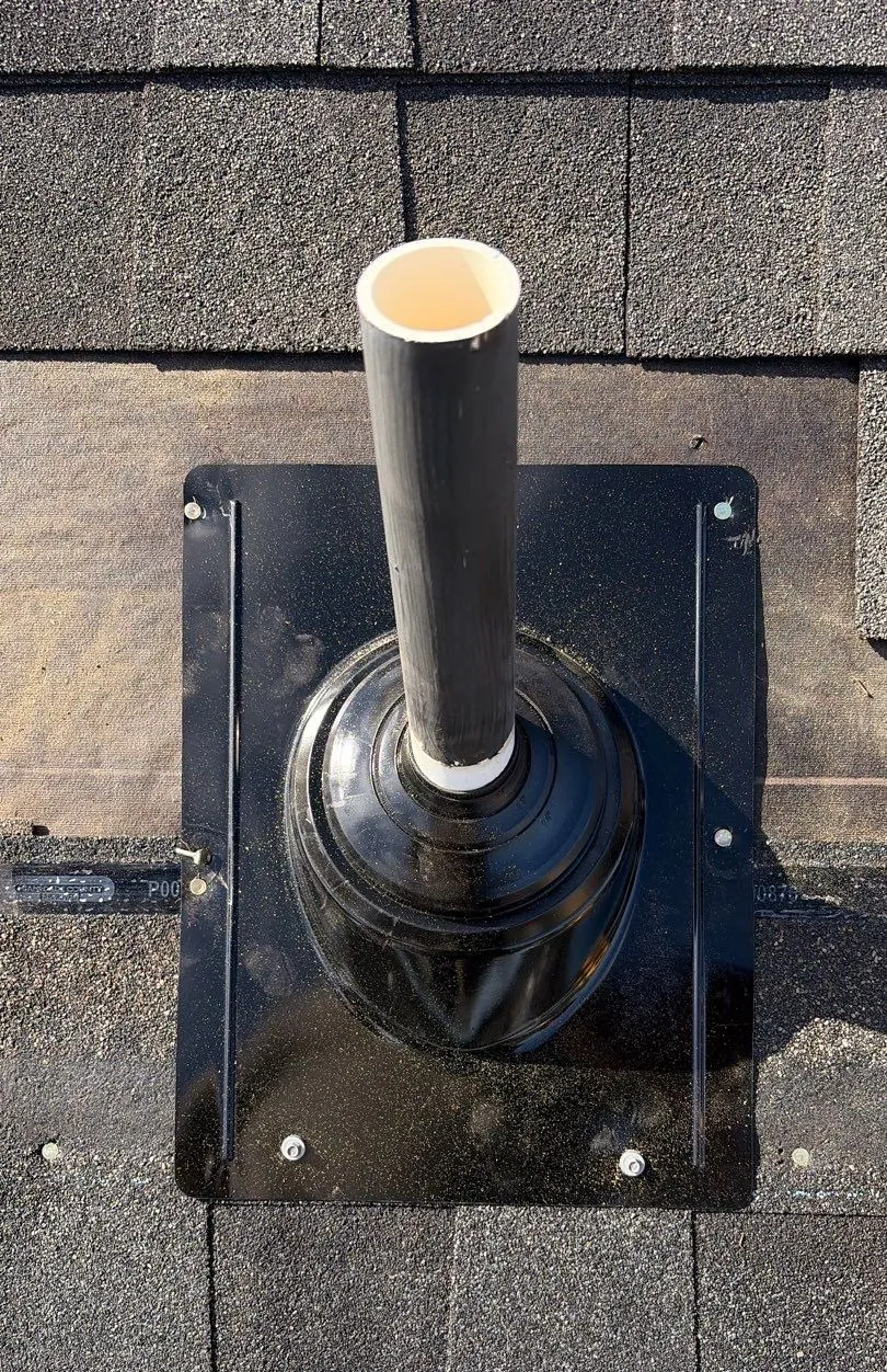 New black pipe jack on a shingle roof with its flange fastened by screws with rubber washers, shingles laid back around it