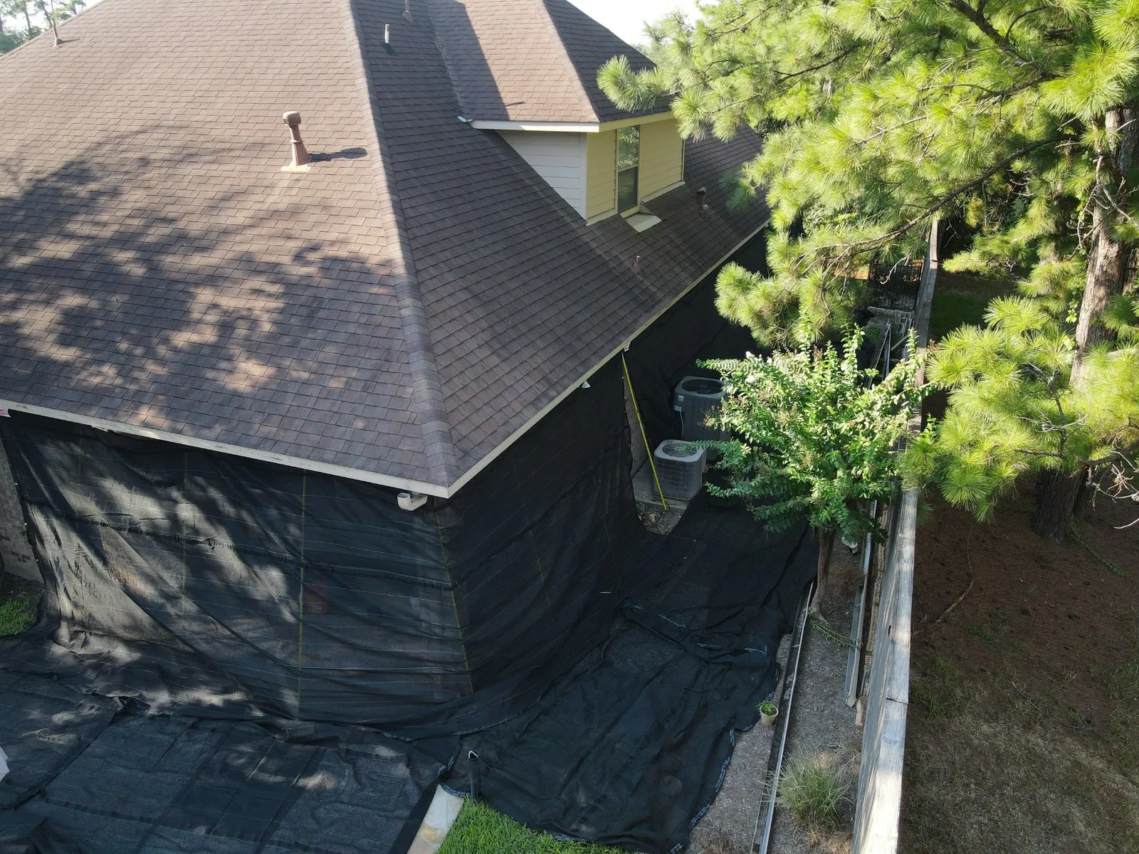 Corner of a home with black netting over the wall and around two outdoor AC units