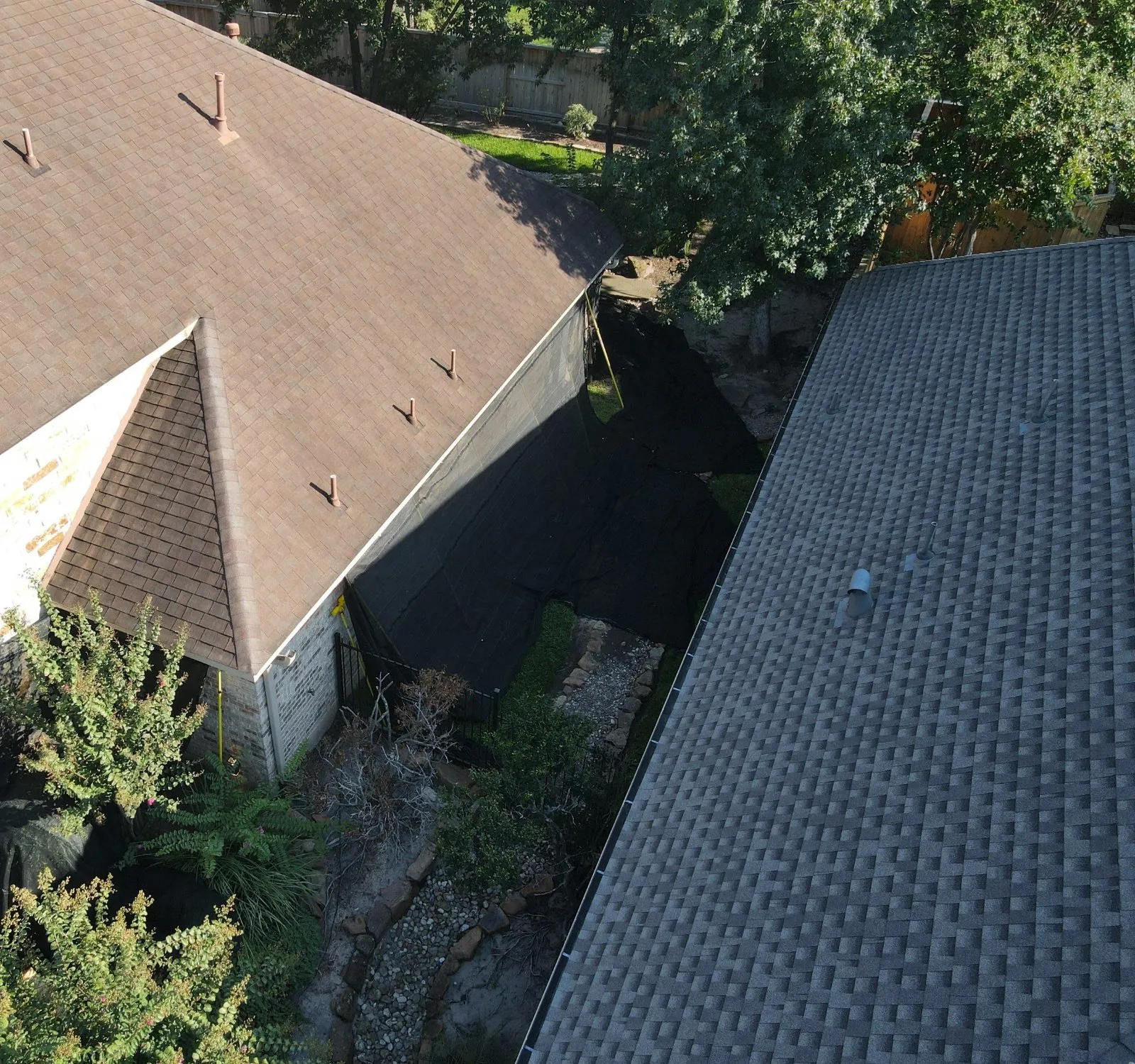 Overhead view of a narrow side yard between two houses, with black netting hung from the roof edge down over the wall and plants