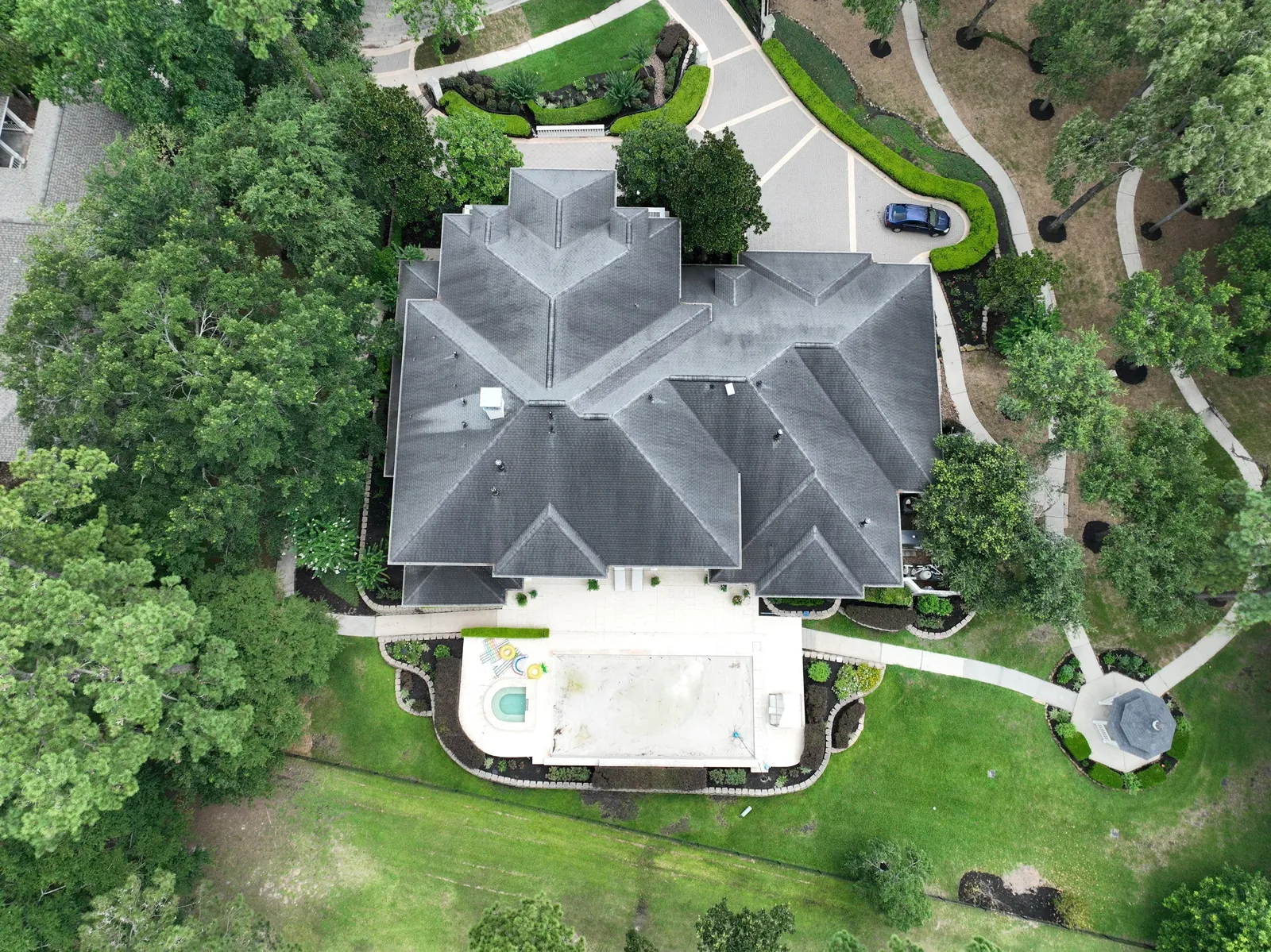 Straight-down aerial view of a large gray shingle roof surrounded by trees, before work started