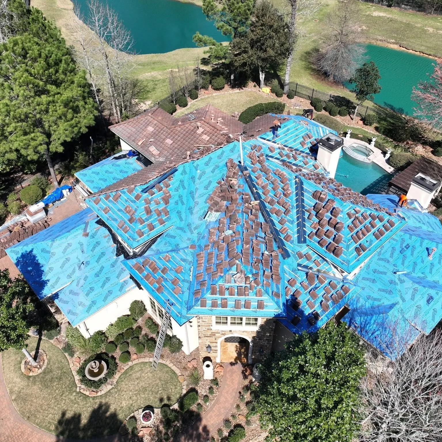 Aerial view of a Spanish tile roof partly stripped, with the good tiles stacked on the roof and new blue underlayment down on the open sections