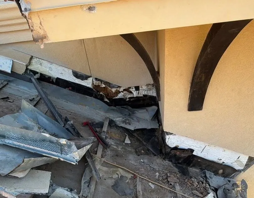Stucco cut open where a tile roof meets the wall, showing torn old flashing and rotted wood behind it